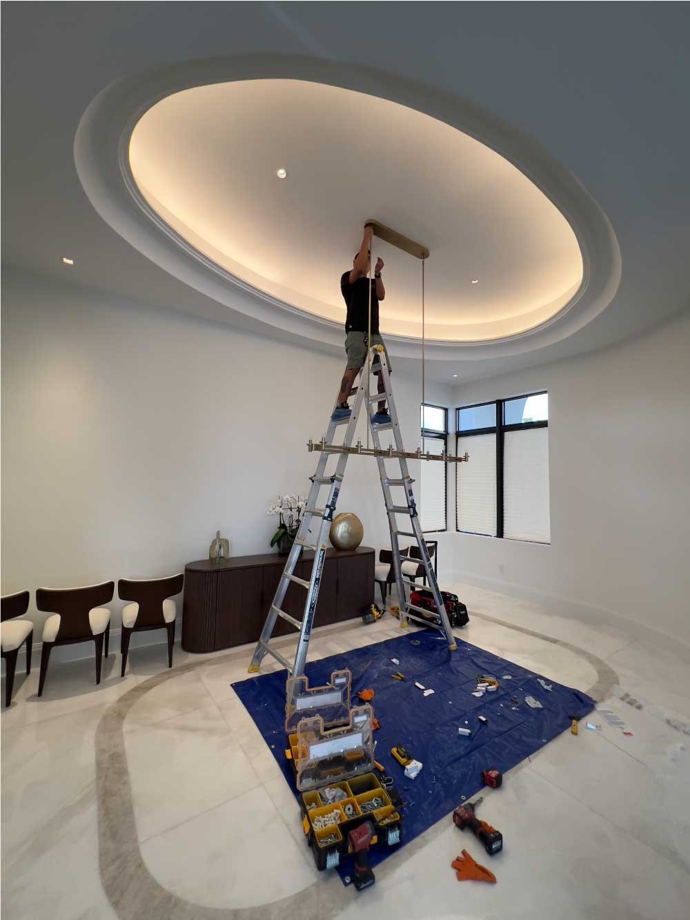 Handyman on a ladder installing cove lighting in a dining room ceiling