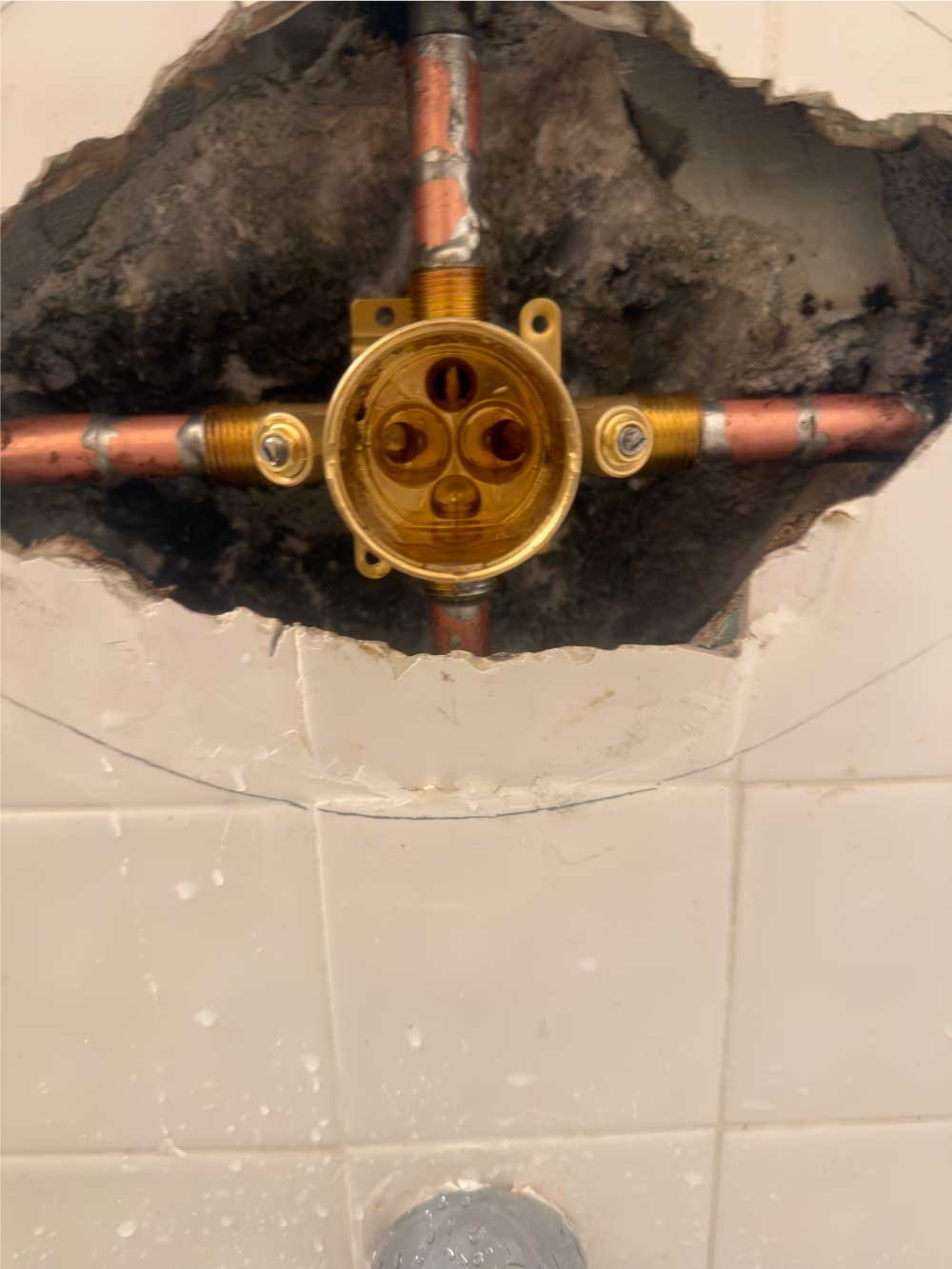 Corroded shower valve exposed in a tile wall before replacement