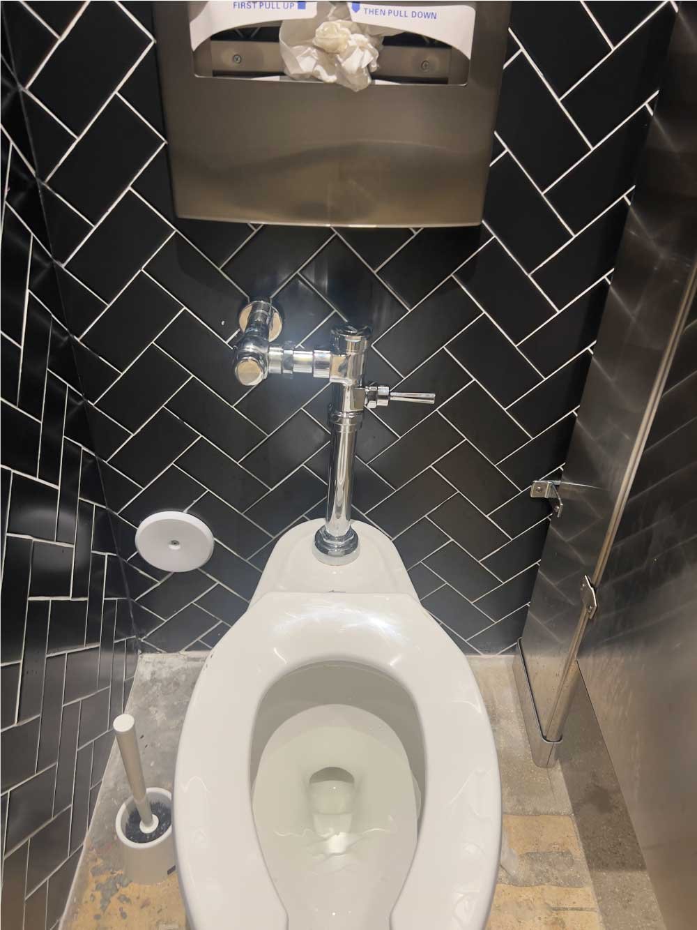 Commercial restroom with black herringbone tile and a new toilet